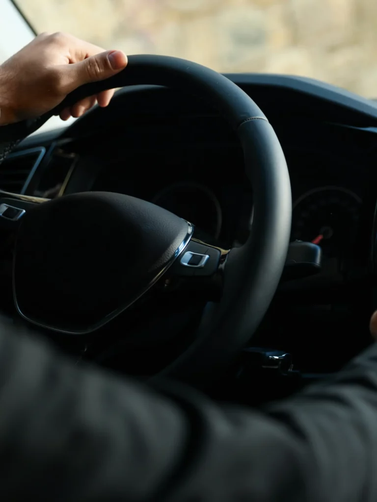 Conducteur tenant le volant dans l'habitacle d'un véhicule, mains sur un volant noir de voiture